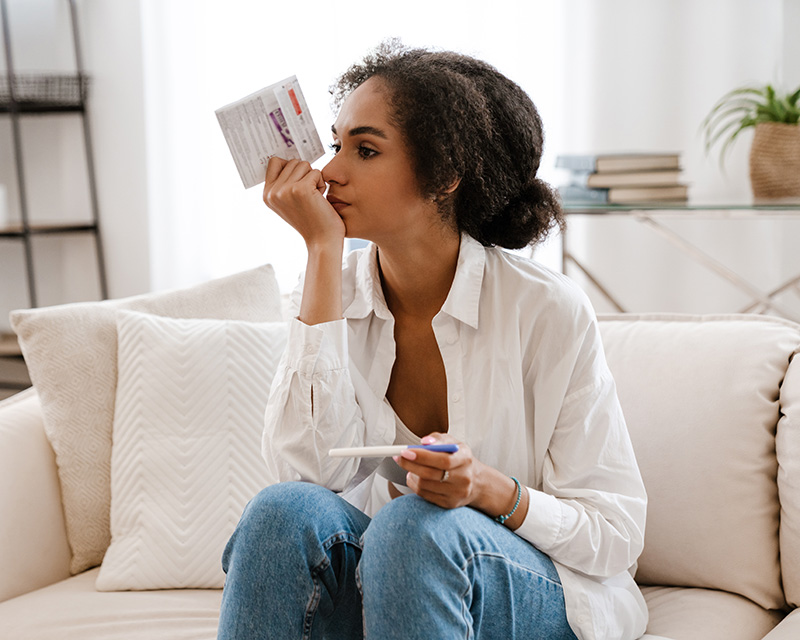 Black woman on a couch holding a pregnancy test, struggling with infertility and needing support